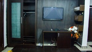 Ein Zimmer mit einem dunklen Holzschrank, einem flachbildfernseher an der Wand und einem Schreibtisch mit Computer und Blumenvase.