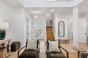 A spacious living area with a staircase, a chandelier, and a large mirror.