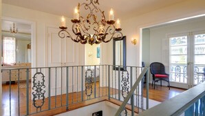 Een ruime kamer met een kroonluchter, een wenteltrap en uitzicht door een glazen deur.