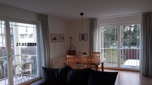 Un salon avec un canapé, une table à manger et des chaises, ainsi que de grandes fenêtres avec des rideaux.