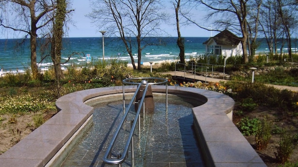 A swimming pool with a metal ladder, surrounded by a stone deck, with a view of the ocean and beach in the background. - Baltic Sea holiday with sea view in a prime location in Göhren on Rügen (Göhren)