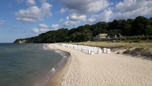 A sandy beach with white containers lined up, a clear sky, and a forested hill in the background. - Baltic Sea holiday with sea view in a prime location in Göhren on Rügen (Göhren)
