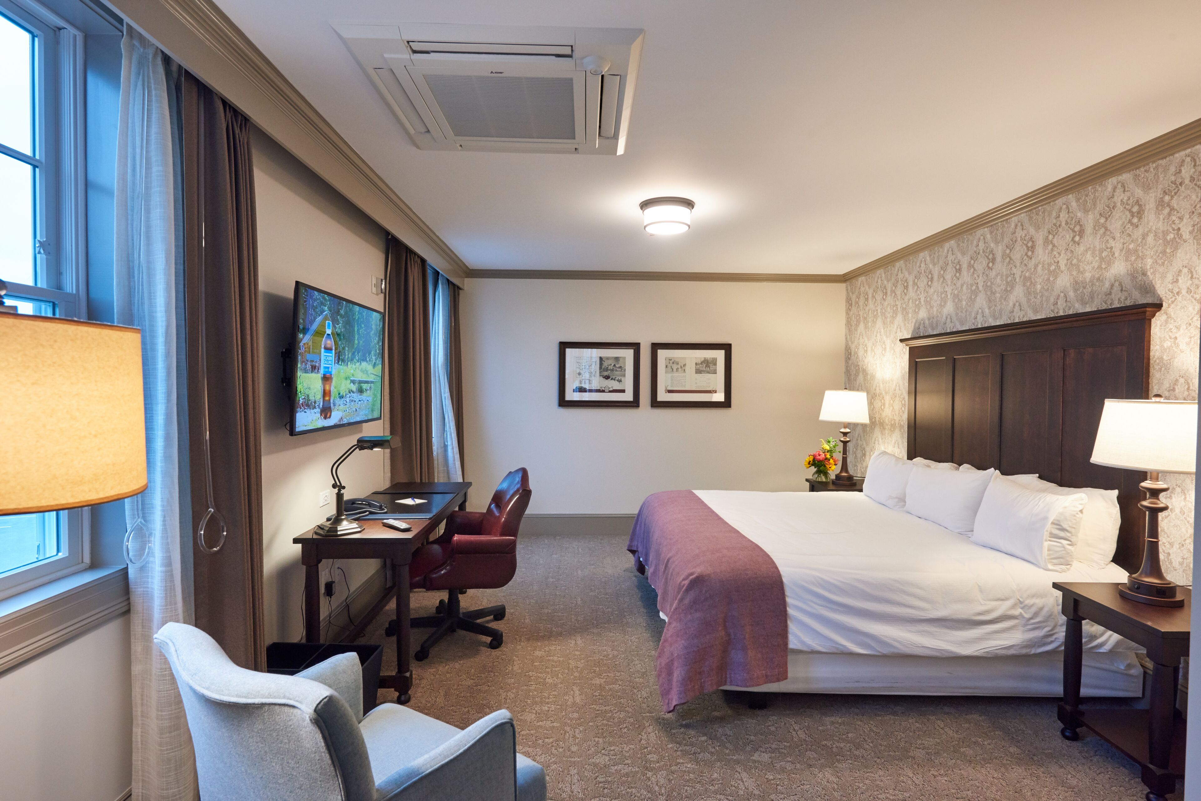 A hotel room with a bed, desk, chair, and a TV on the wall.