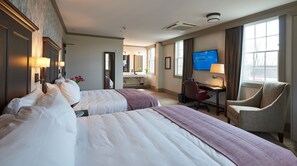Une chambre d’hôtel avec deux lits, un bureau, une chaise, une télévision et une salle de bain visible au fond.