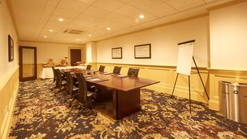 A conference room with a large table, chairs, a whiteboard, and a recycling bin.