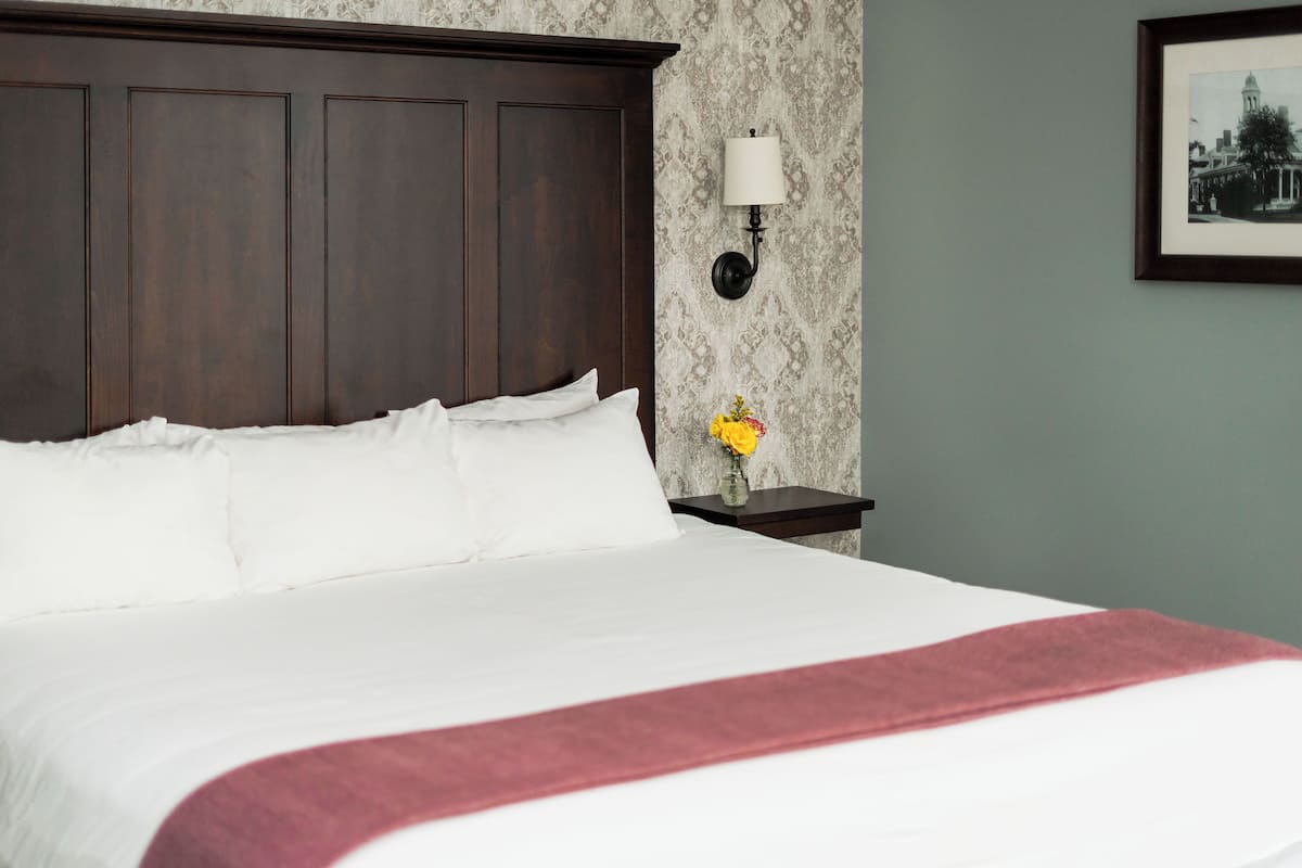 A neatly made bed with white linens and a red throw blanket, a dark wooden headboard, a nightstand with a lamp, and a framed picture on the wall.