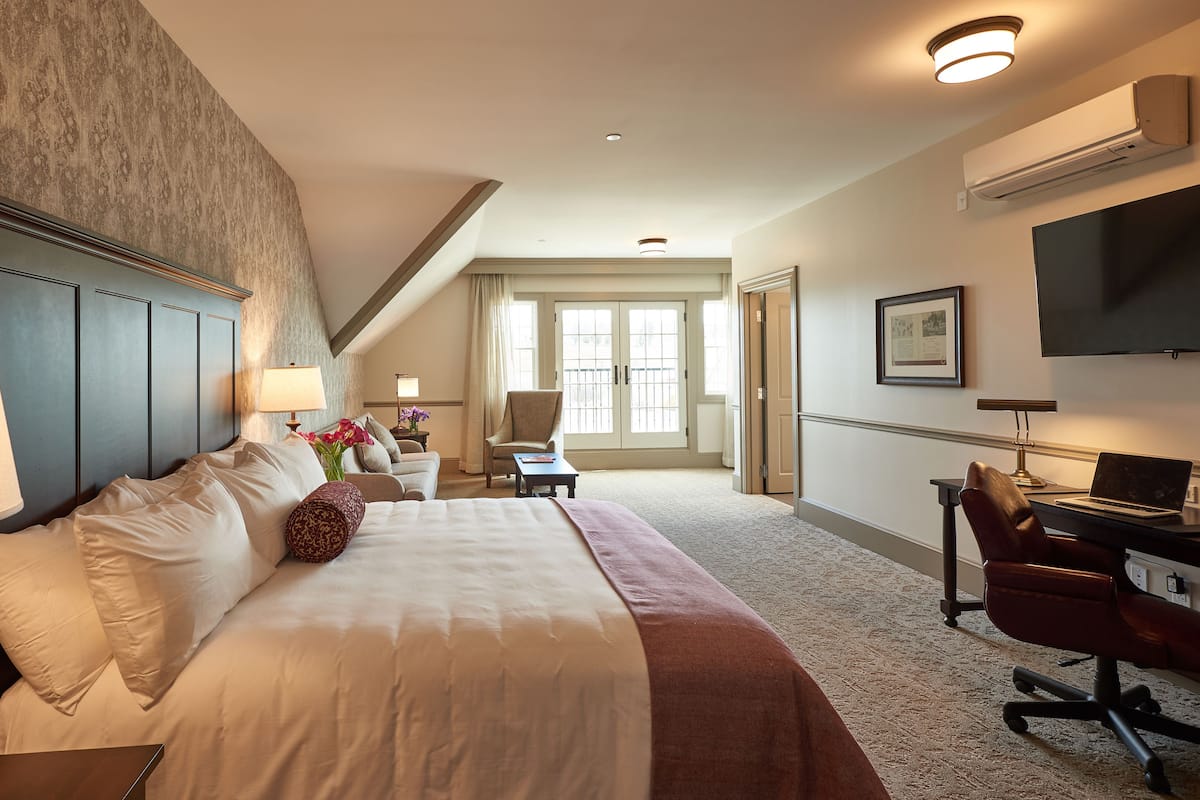 A hotel room with a large bed, a desk with a laptop, a chair, a TV, and a window with curtains.