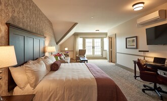 Quarto de hotel com uma cama grande, uma escrivaninha com um laptop, uma cadeira, uma televisão e uma janela com cortinas.