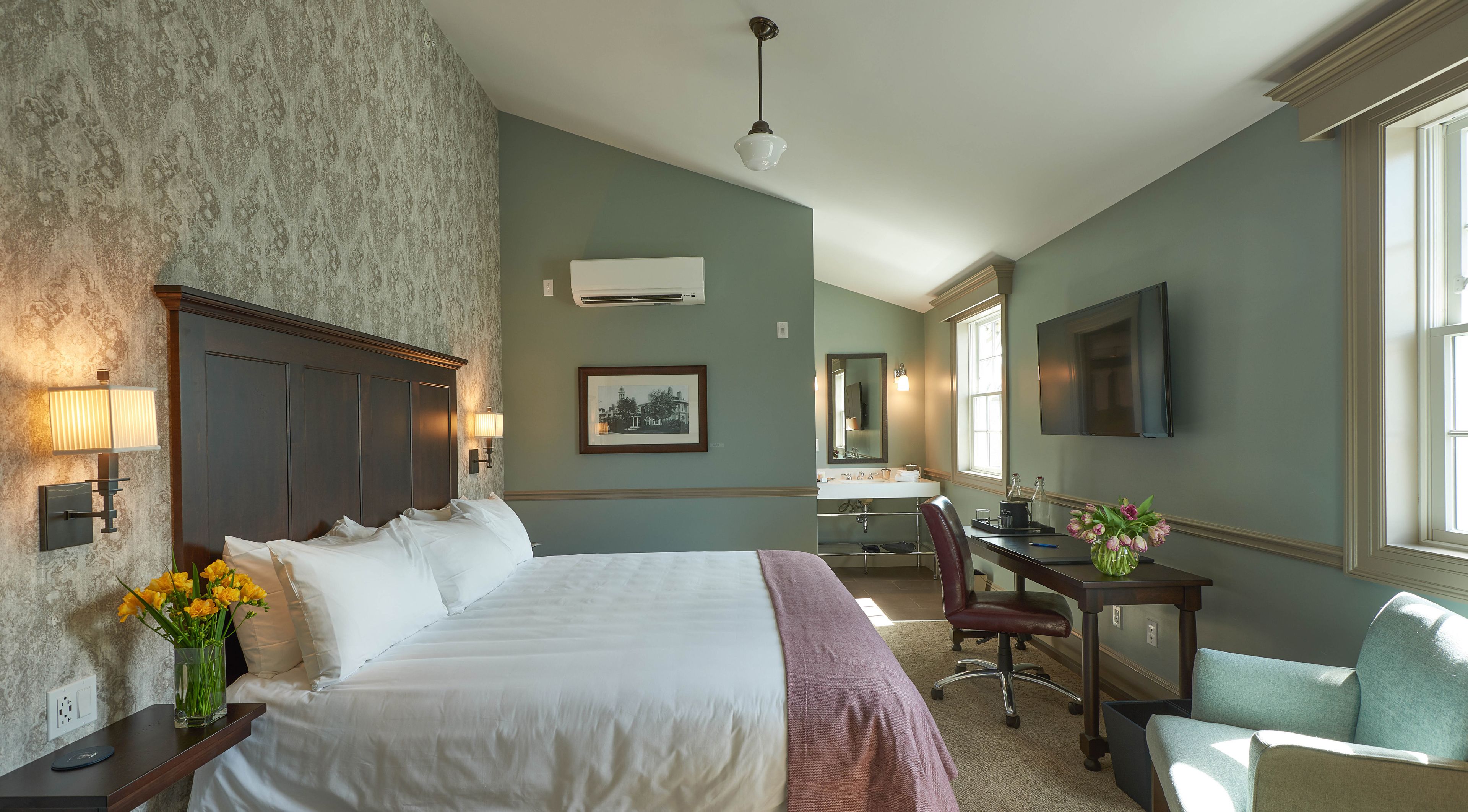A hotel room with a large bed, a desk, a chair, a TV, and a window.