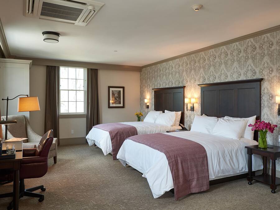 A hotel room with two beds, a desk, a chair, a TV, and a window with curtains.