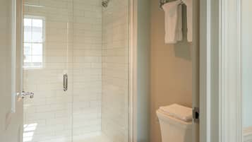 A bathroom with a glass-enclosed shower, white tiled walls, a toilet, and a towel rack.