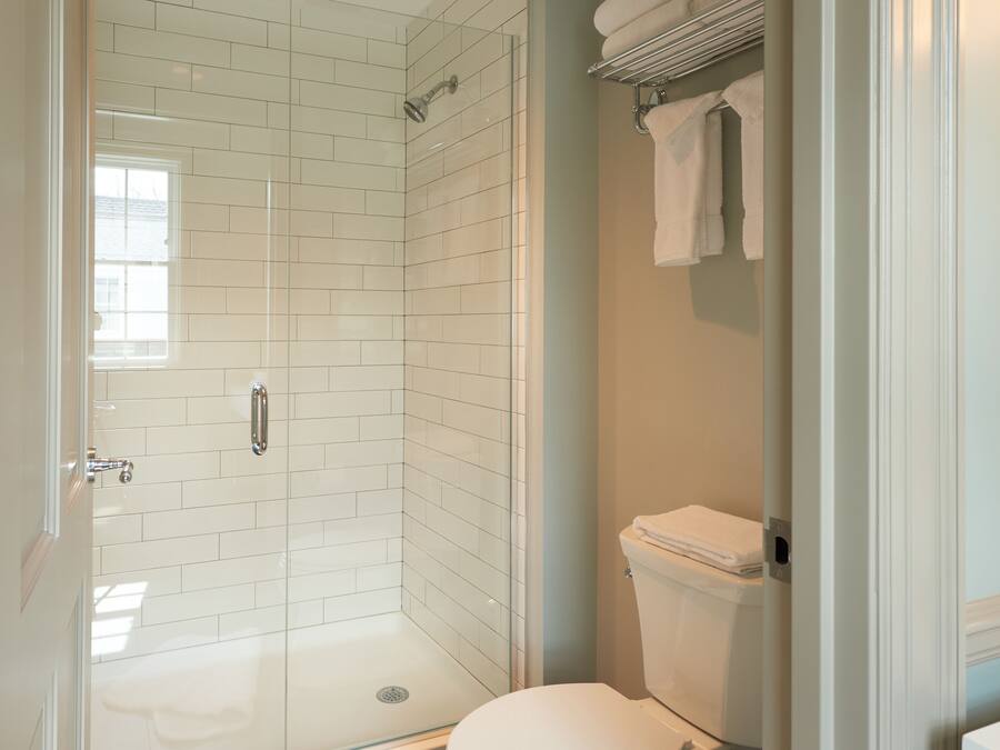 A bathroom with a glass-enclosed shower, white tiled walls, a toilet, and a towel rack.