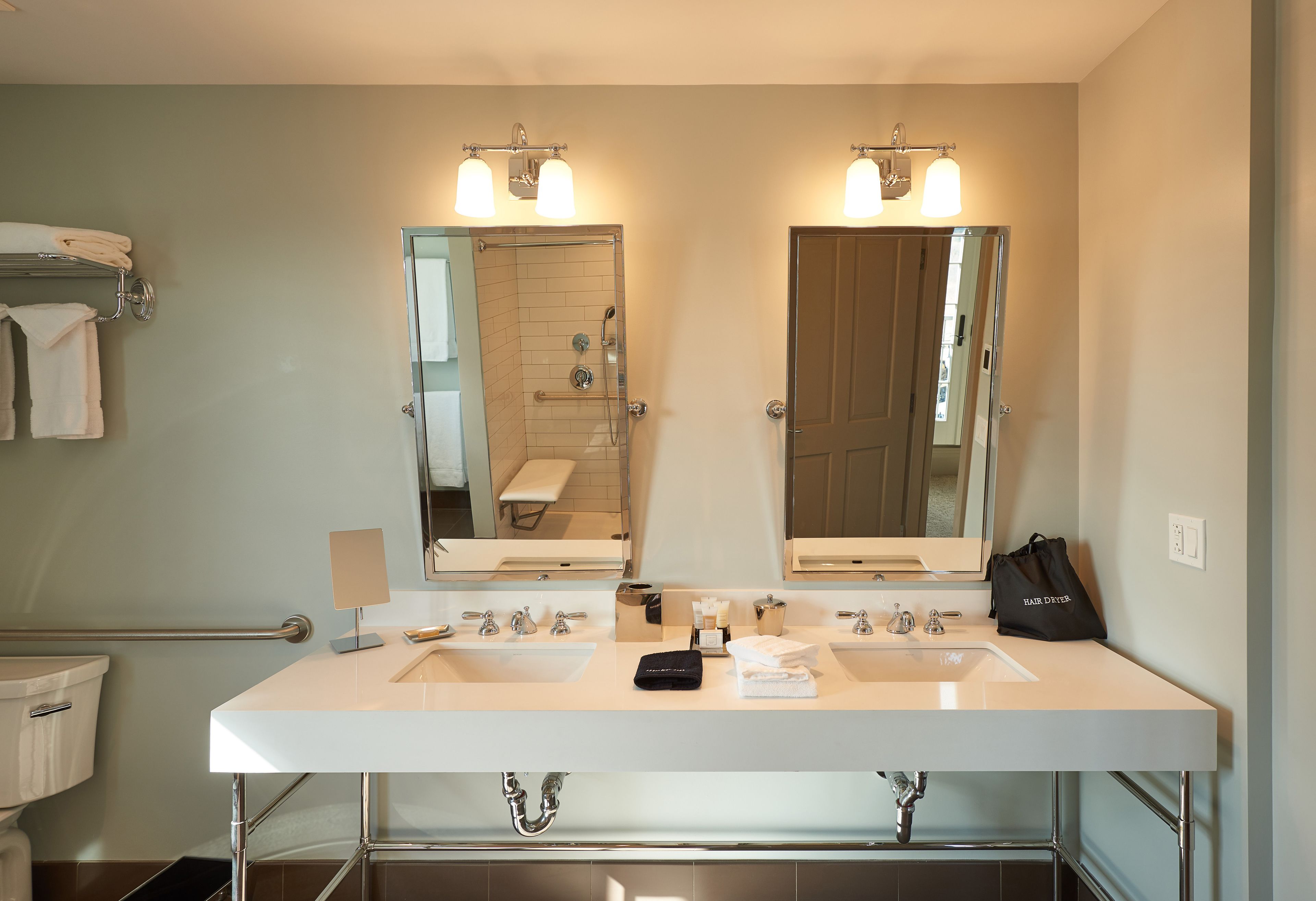 A hotel bathroom with two sinks, a mirror, and a towel rack.