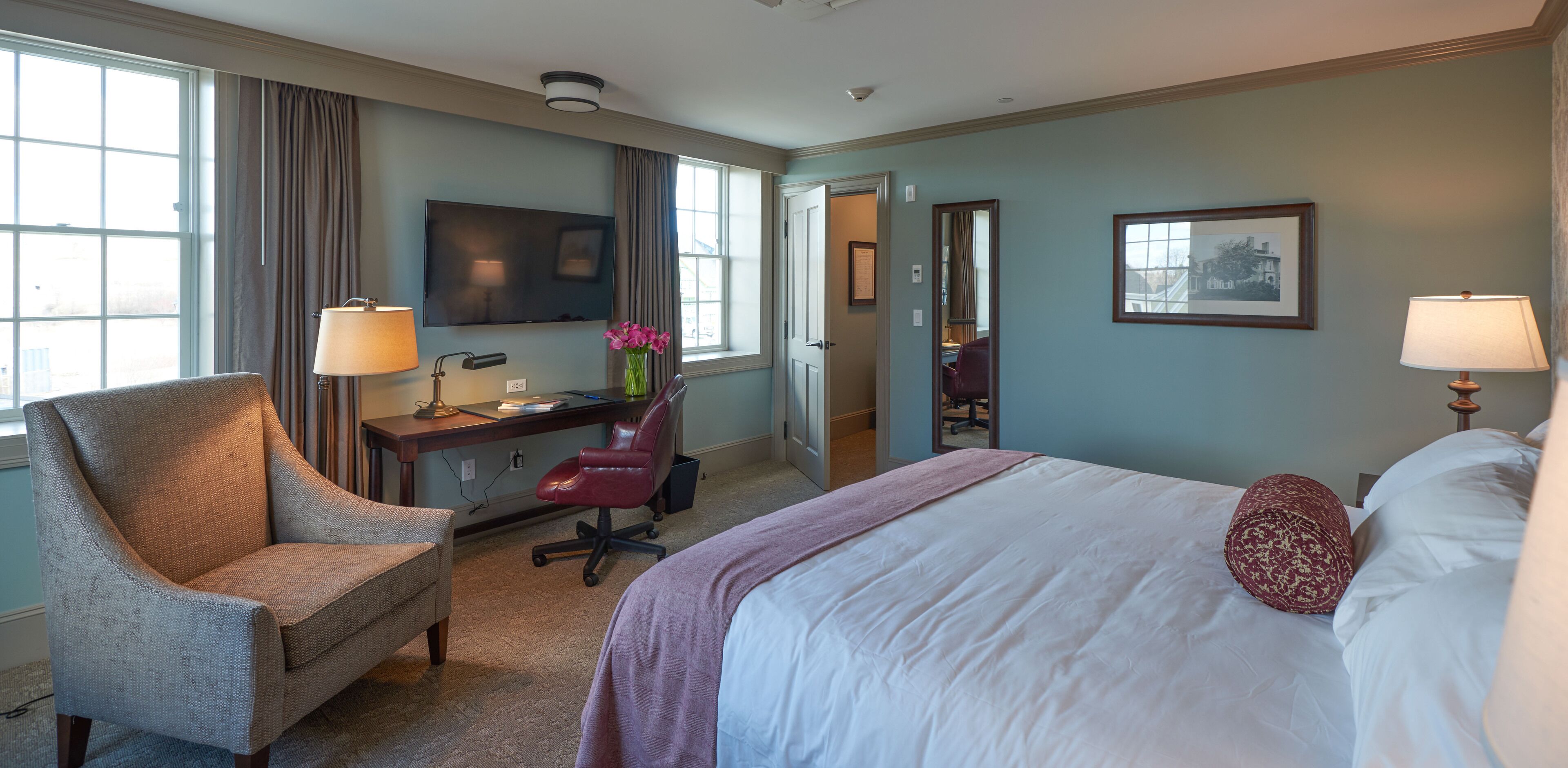 Habitación de hotel con cama, escritorio, silla, televisión y ventana con cortinas.