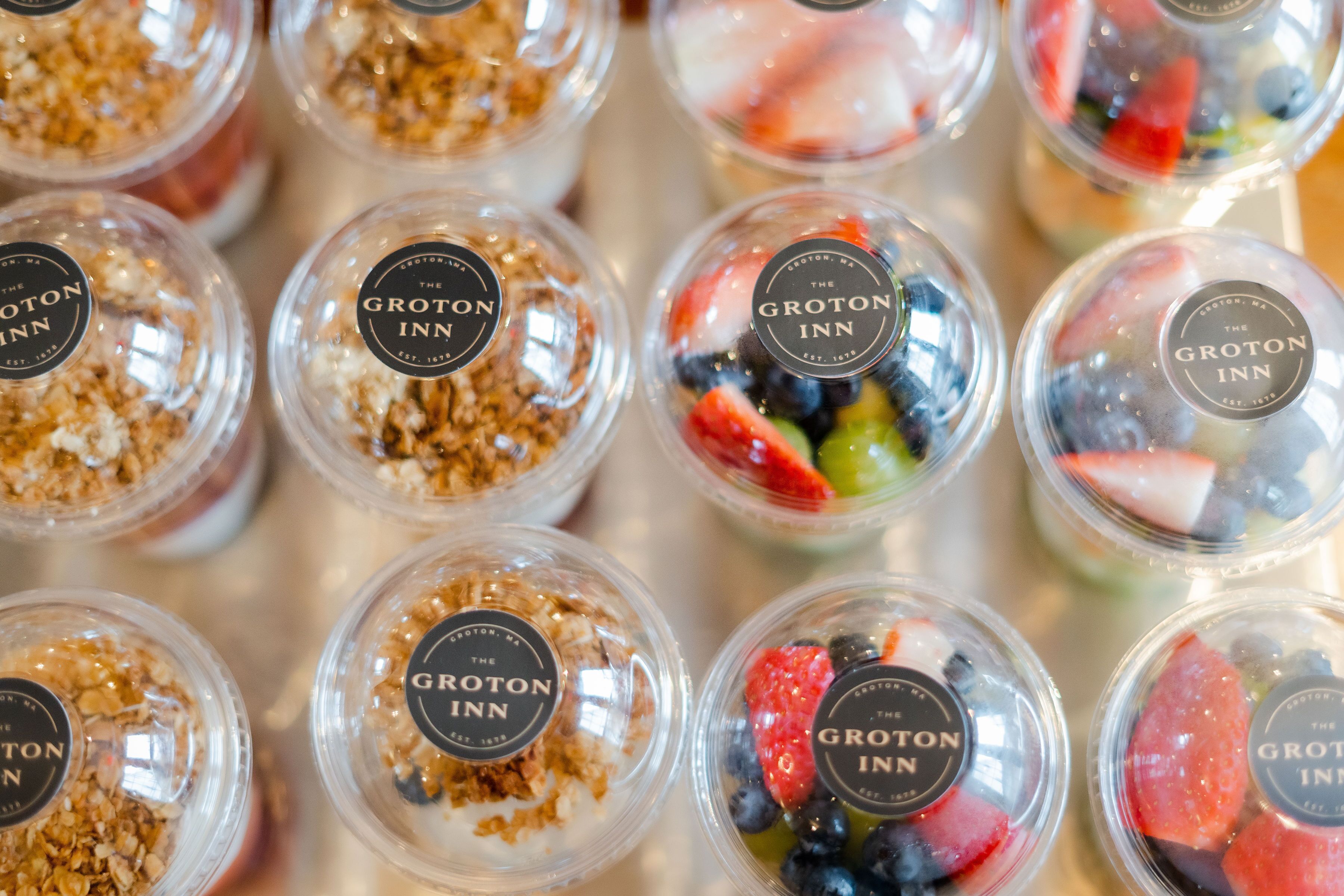 Multiple clear plastic cups with labels, each containing different types of food.