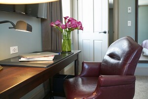 Ein Zimmer mit Schreibtisch, Laptop, Blumen in einer Vase und einem Ledersessel.