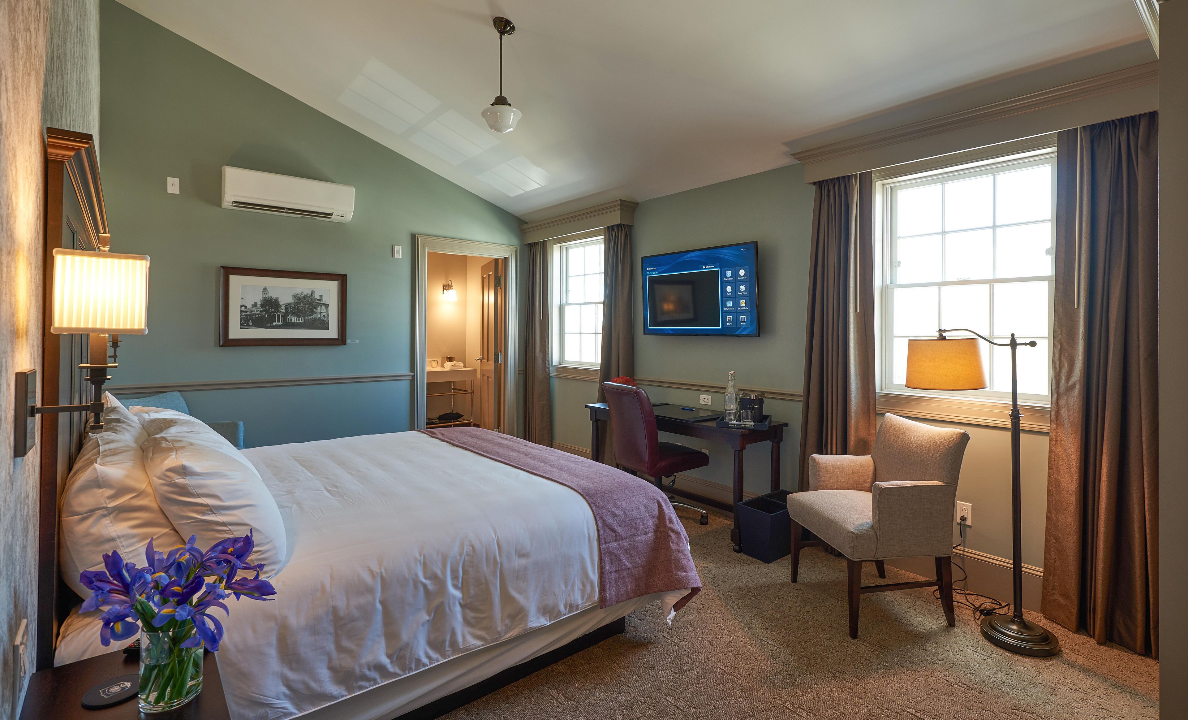 A hotel room with a bed, desk, chair, TV, and a window with curtains.