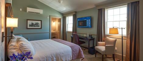 A hotel room with a bed, desk, chair, TV, and a window with curtains.