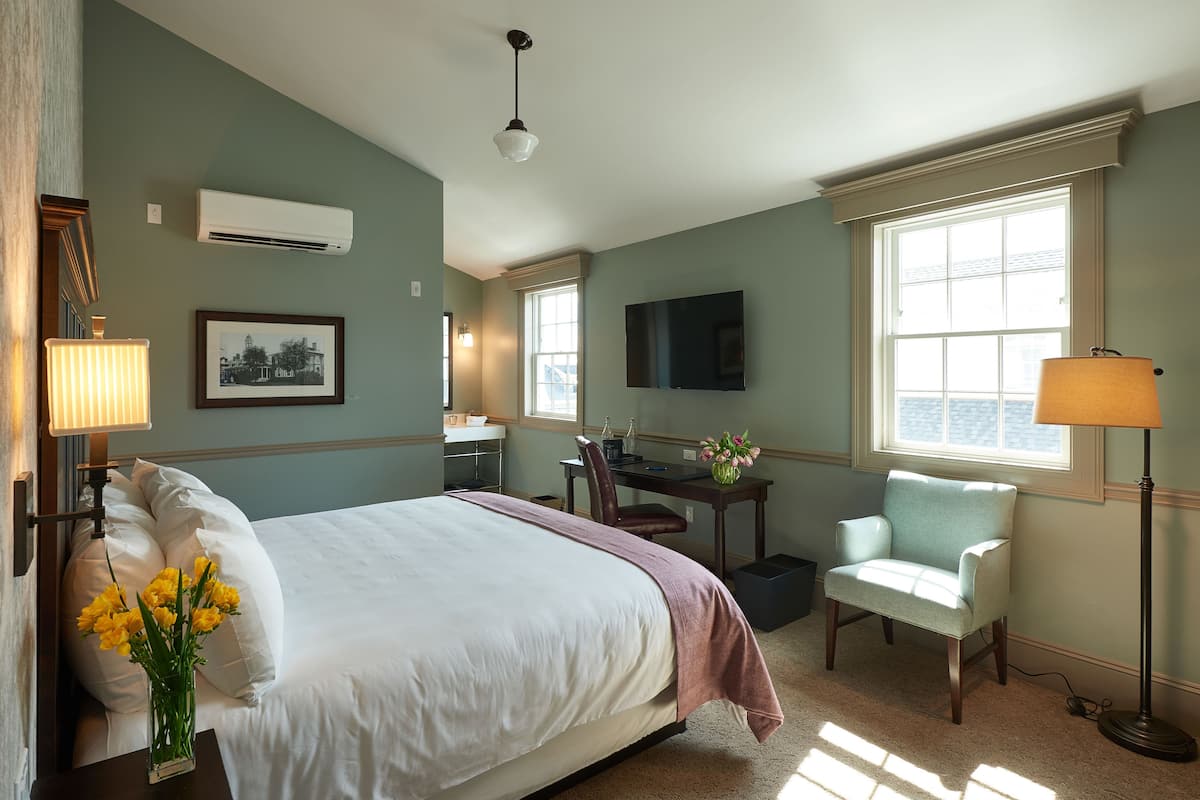 A hotel room with a bed, a desk, a chair, a TV, and a window.