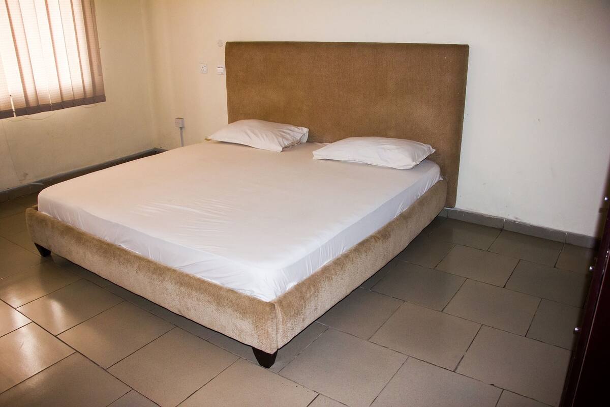 A single-bed room with a beige headboard, white bedding, and a tiled floor.