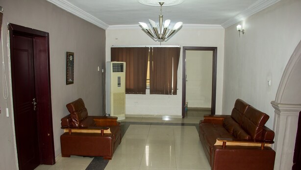A spacious living room with two leather sofas, a chandelier, and a large window with curtains. - David Royal Suites (Lagos)