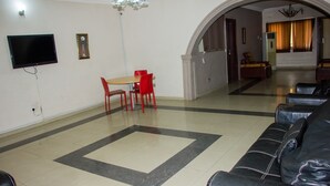 A living room with a black leather sofa, a dining table with red chairs, a flat-screen TV, and a chandelier. - David Royal Suites (Lagos)