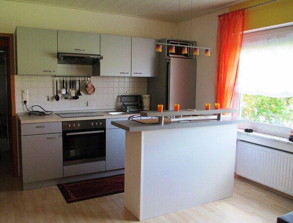 A modern kitchen with a central island, built-in oven, and stainless steel appliances. - Apartment right on the forest in a quiet, secluded location in the heart of the Vulkaneifel (Gerolstein)