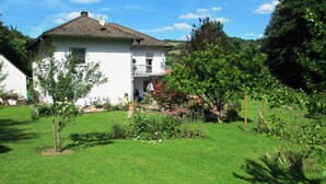 A two-story house with a balcony, surrounded by a well-maintained garden with various plants and flowers. - Apartment right on the forest in a quiet, secluded location in the heart of the Vulkaneifel (Gerolstein)