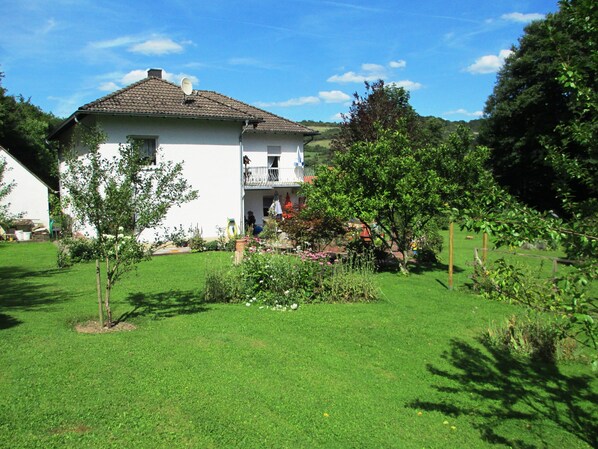 A two-story house with a balcony, surrounded by a well-maintained garden with various plants and flowers.