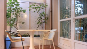 Een klein binnenhofje met een witte tafel en twee stoelen, omringd door grote ramen en planten in potten.
