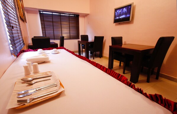 Una sala conferenze con un lungo tavolo apparecchiato per un pasto, completa di sedie e un televisore appeso al muro.