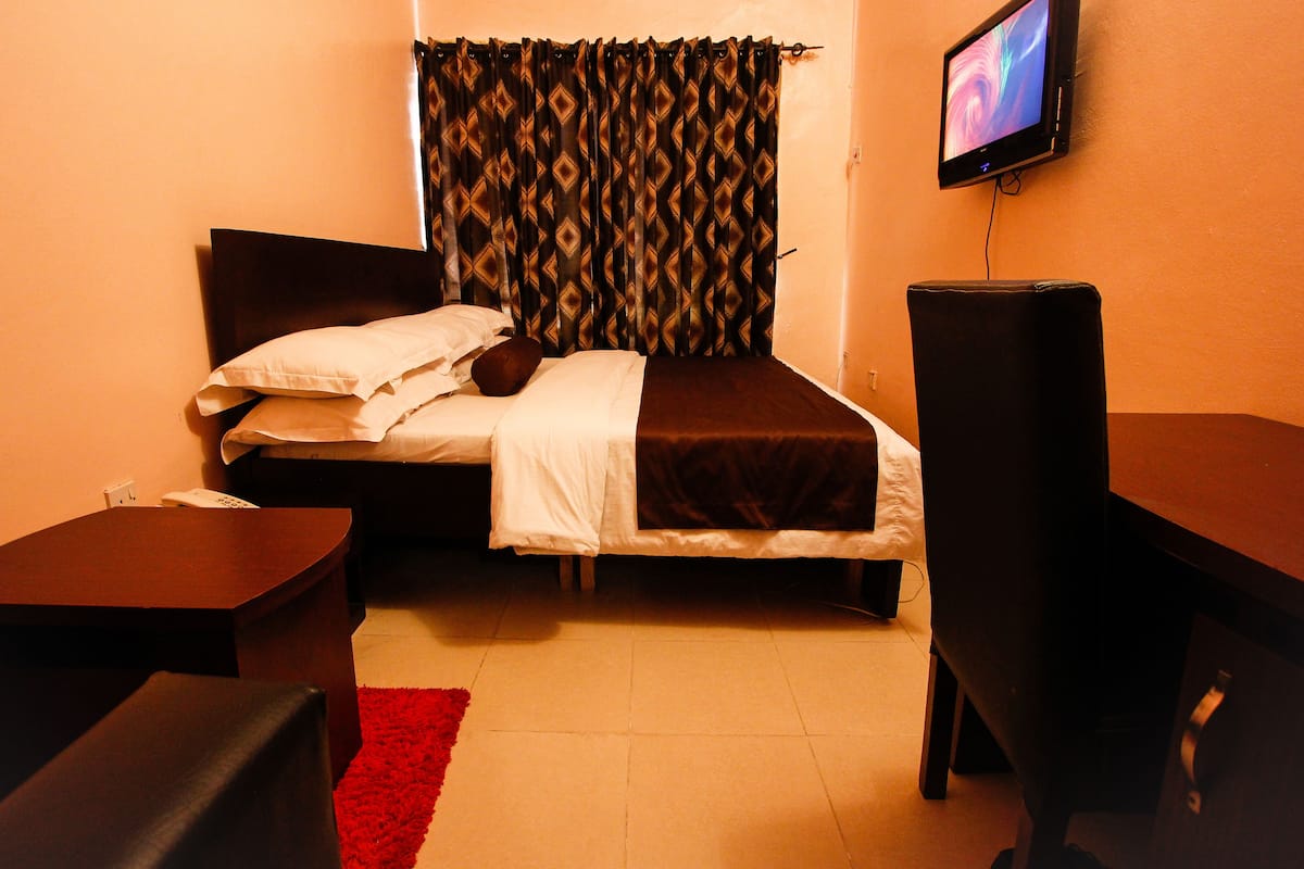 Quarto com uma cama, televisão, escrivaninha e tapete vermelho.