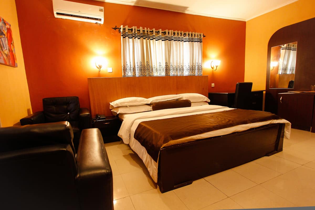 Quarto de hotel com uma cama grande, duas mesas de cabeceira, uma cadeira, uma escrivaninha e um espelho.