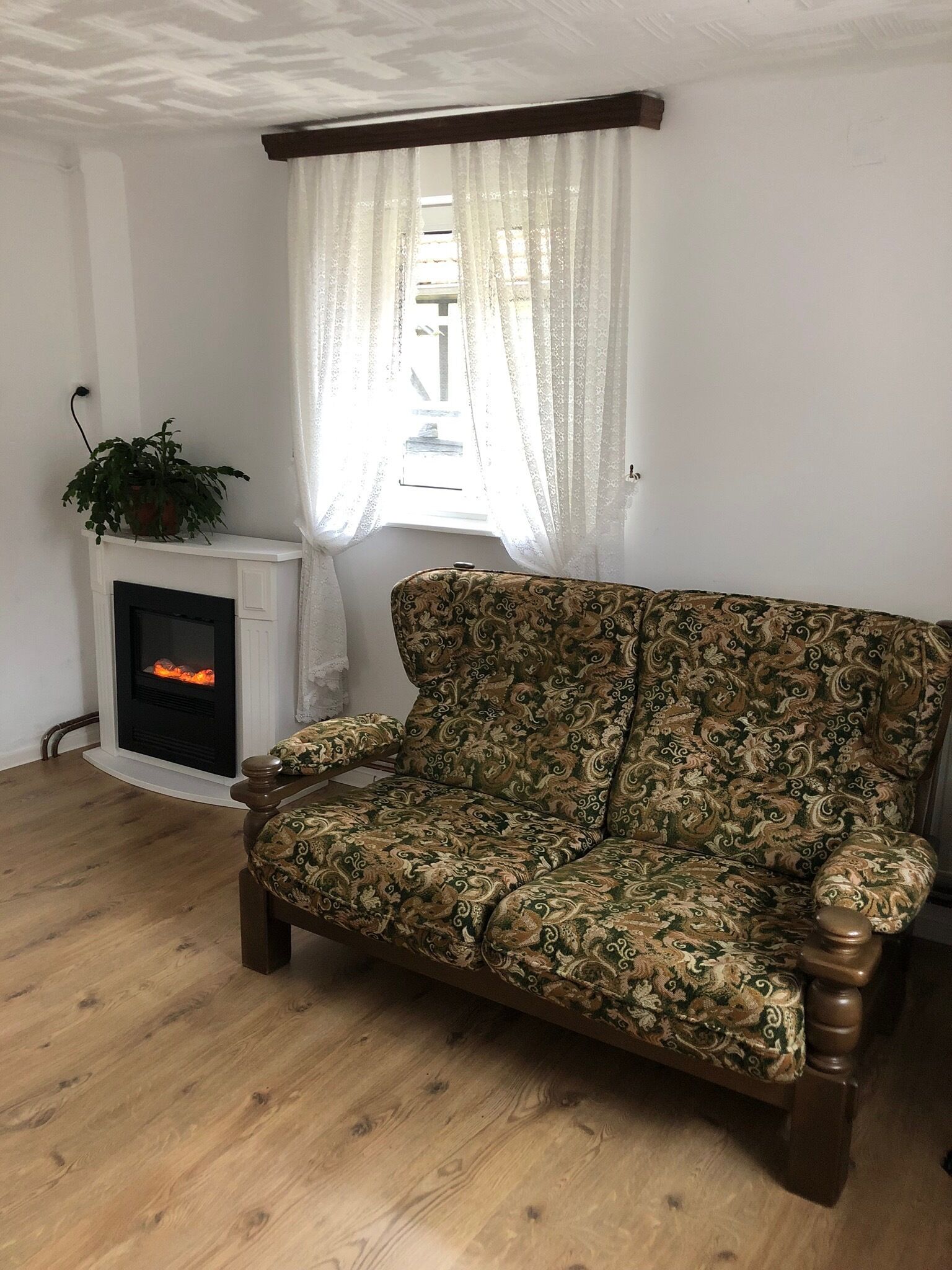 A living room with a patterned sofa, a fireplace, and a window with sheer curtains.