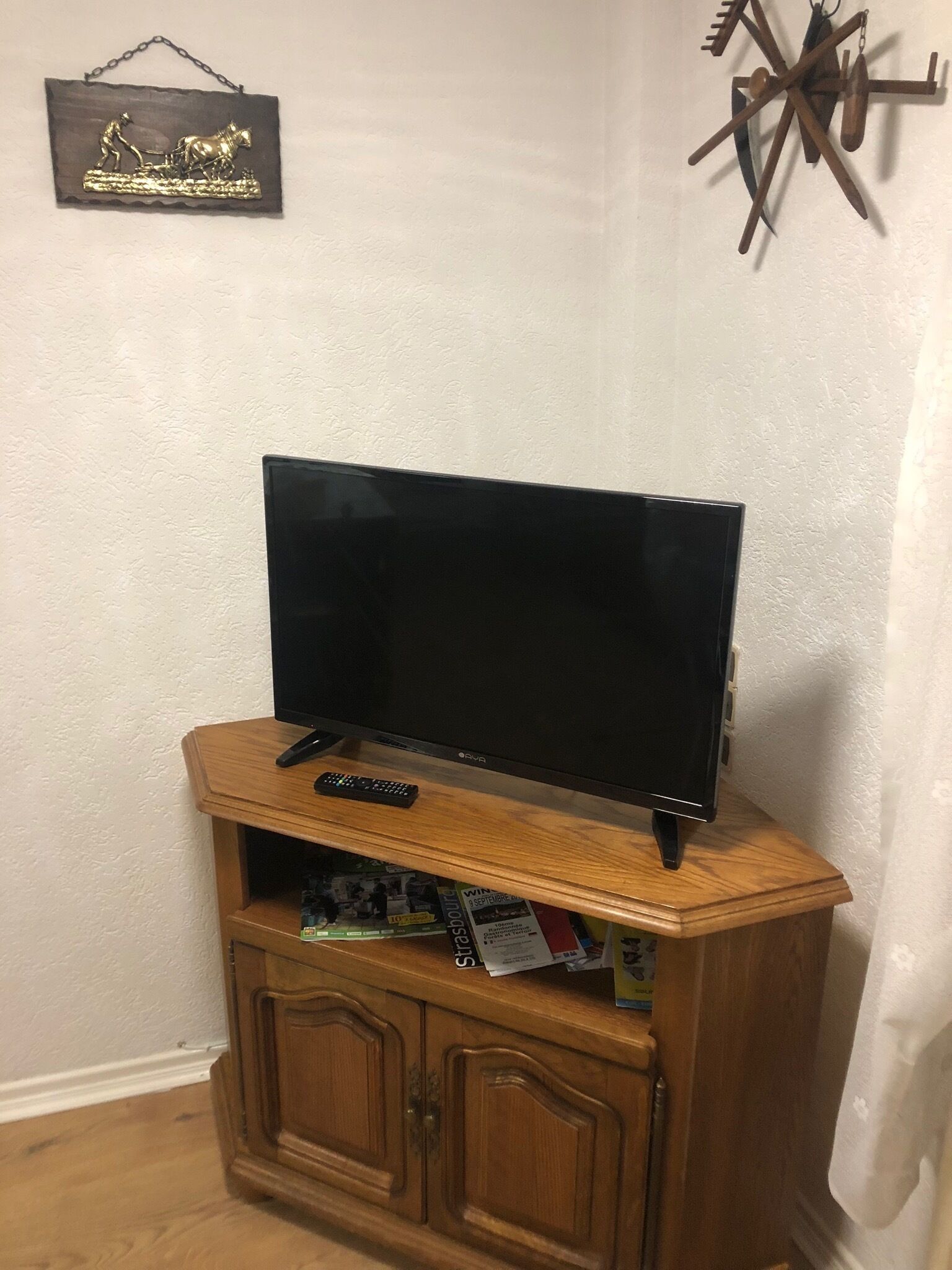 Ein Fernseher auf einem Holzboden mit Fernbedienung, einem kleinen Schrank darunter und einem dekorativen Gegenstand an der Wand.