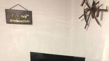 Ein Fernseher auf einem Holzboden mit Fernbedienung, einem kleinen Schrank darunter und einem dekorativen Gegenstand an der Wand.