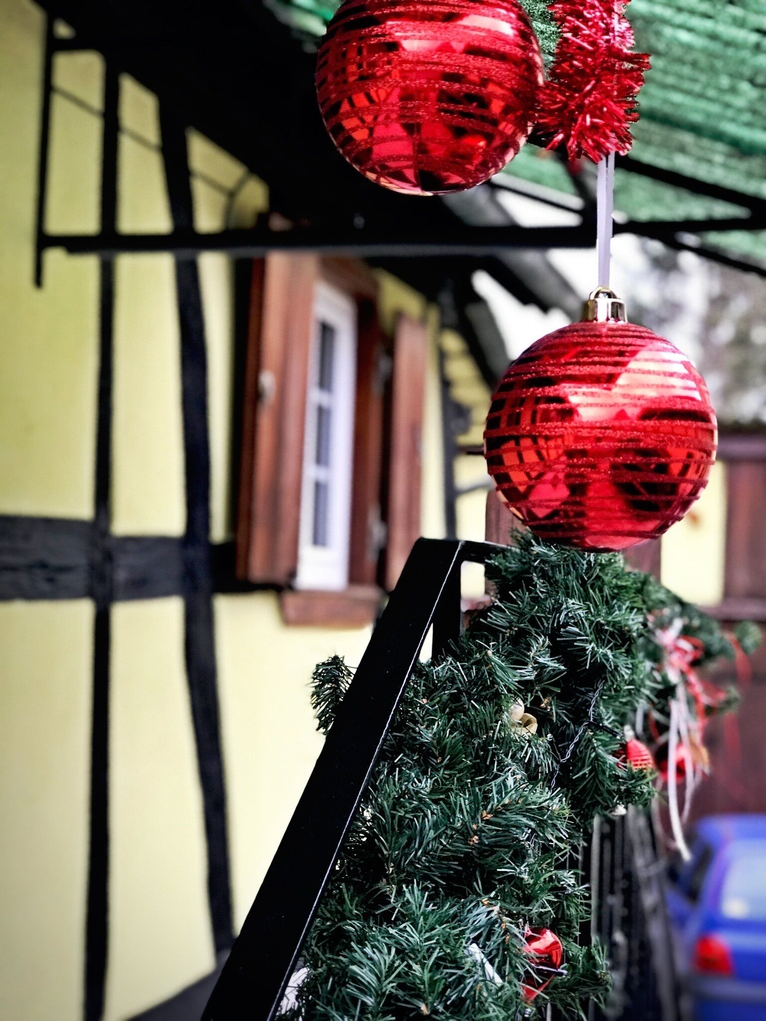 Ein Weihnachtsbaum mit roten Verzierungen und einem schwarzen Fuß, vor einem gelben Gebäude mit schwarzer Verzierung.