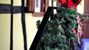 Ein Weihnachtsbaum mit roten Verzierungen und einem schwarzen Fuß, vor einem gelben Gebäude mit schwarzer Verzierung.