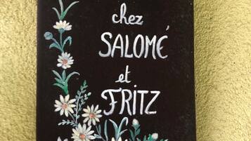 Een zwart bord met witte tekst en bloemversiering, waarop staat 'BIENVENUE chez SALOME et FRIZ'.