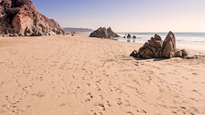 A sandy beach with large rock formations and footprints.