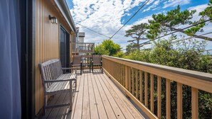 A wooden deck with a bench and chairs, a balcony with a railing, and a view of trees and sky.