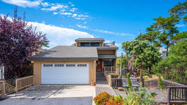 A two-story house with a garage, wooden deck, and a variety of plants.