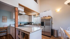 A modern kitchen with white cabinets, a stainless steel refrigerator, a microwave, and a wooden island with a granite countertop.