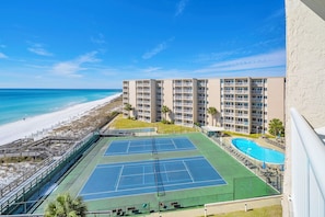 Ein Tennisplatz mit Pool, Strand und einem Gebäude mit Balkonen.