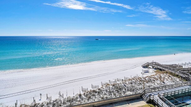 A beach with a wooden boardwalk leading to a building with a glass facade. - 622- Set your clock to Beach time! Renovated, high end Condo, stunning views (Destin)
