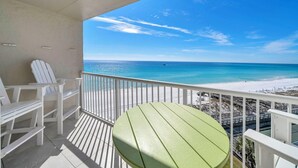 A balcony with white chairs and a green table, overlooking a beach with clear blue water and a distant boat. - 622- Set your clock to Beach time! Renovated, high end Condo, stunning views (Destin)