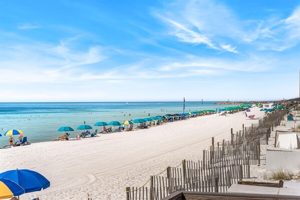Ein Strand mit Reihen von Sonnenschirmen und Liegestühlen, einem Holenzaun und freiem Blick auf den Ozean.