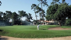 Un campo de golf con un green de putting, árboles y un edificio al fondo.