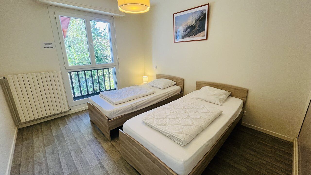 A bedroom with two single beds, a window with a view of greenery, a radiator, and a framed picture on the wall.