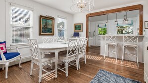 Ein Essbereich mit weißem Tisch und Stühlen, einer Chandelierleuchtre und Kunstwerken an den Wänden.